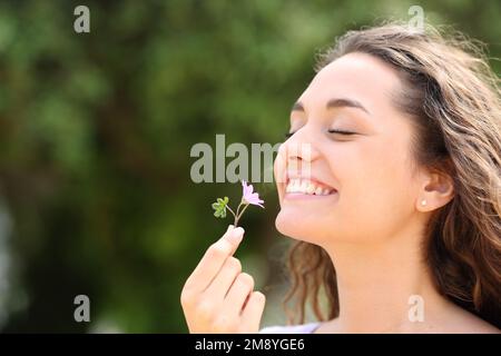 Felice donna candida che odora piccolo fiore in un parco Foto Stock