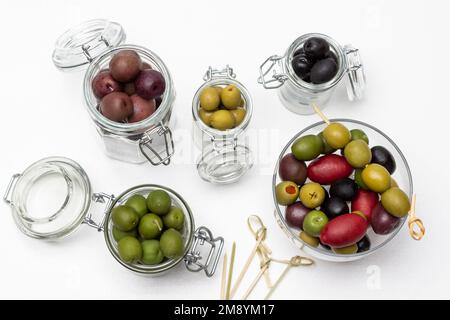 Olive in vasetti di vetro. Spiedini sul tavolo. Giacitura piatta. Sfondo bianco. Foto Stock