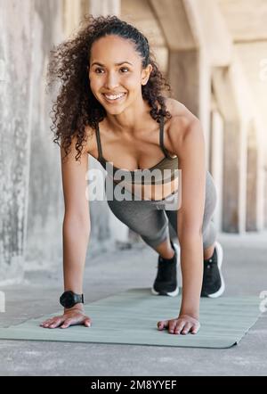 Spingendolo con un sorriso. Scatto a tutta lunghezza di una giovane donna attraente che fa i pushups durante il suo workout all'aperto nella città. Foto Stock