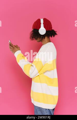 Giovane uomo caraibico in cuffie con cellulare isolato su sfondo rosa Foto Stock