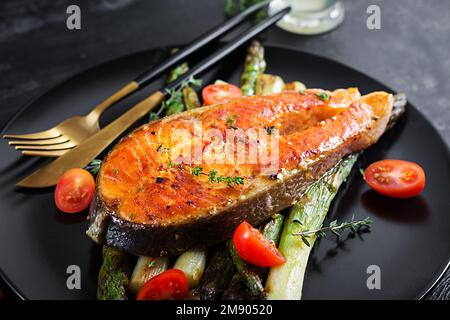 Salmone arrosto guarnito con asparagi e pomodori con erbe aromatiche. Pranzo chetogenico. Dieta Keto Foto Stock