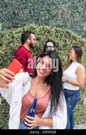 Donna latina che prende un selfie vicino agli amici Foto Stock