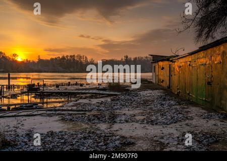 Barche da pesca garage in un porto turistico su un fiume ghiacciato durante una bella alba Foto Stock