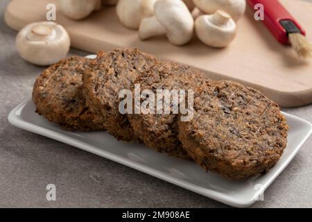 Piatto con hamburger di champignon appena sfornati e funghi freschi sullo sfondo Foto Stock