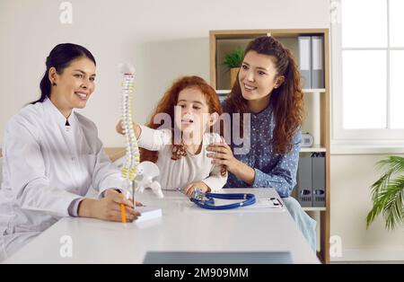 Madre e bambino felici che guardano il modello ortopedico della colonna vertebrale durante la visita all'ufficio del medico Foto Stock