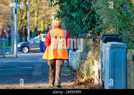 Postino della posta reale che cammina per strada sul suo giro sotto il sole Foto Stock