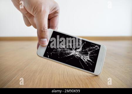 Persona che picking smartphone rotto con schermo rotto sul pavimento a casa Foto Stock