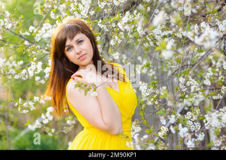 giovane ragazza carina in abito giallo in primavera su sfondo ciliegio fiore Foto Stock