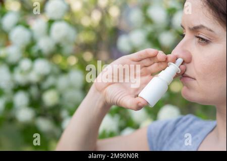 La donna caucasica usa uno spray nasale mentre cammina nel parco. Foto Stock