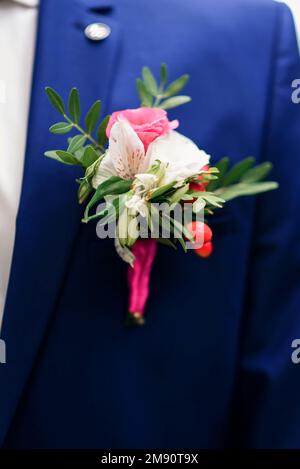 elegante boutonniere di rose bianche e rosa sulla giacca blu dello sposo Foto Stock