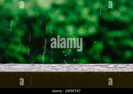 Scatto cinematografico di gocce di pioggia che cadono dal cielo grigio e sulla superficie bagnata di una ringhiera del balcone, creando increspature nell'acqua ferma Foto Stock