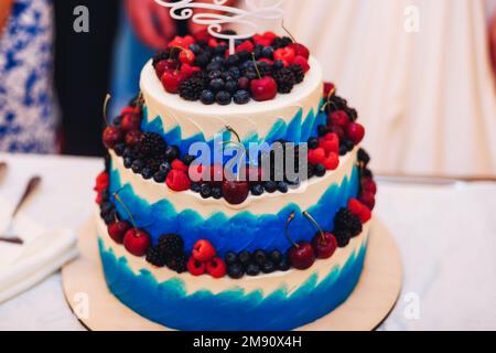 torta nuziale in glassa bianca blu con ciliegie di bacche fresche, mirtilli, more, lamponi a tre livelli Foto Stock