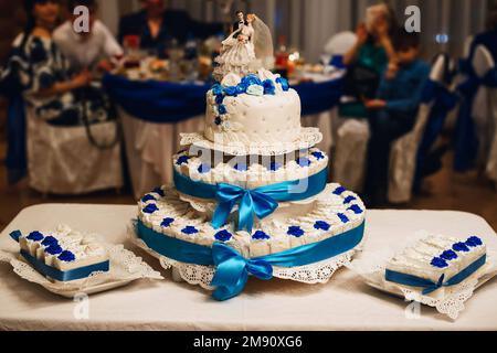 torta bianca di nozze decorata con rose blu con tre piani e torte e una figura della sposa e dello sposo Foto Stock