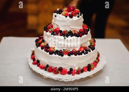 torta nuziale bianca con fragole dolci fresche, ciliegie, mirtilli, ribes nero a tre livelli Foto Stock