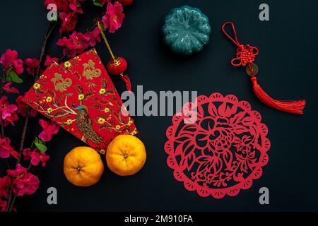 Decorazione cinese lunare di Capodanno su sfondo nero. Concetto piatto con mandarino, busta rossa, fiore di prugna e decorazione festosa. Foto Stock