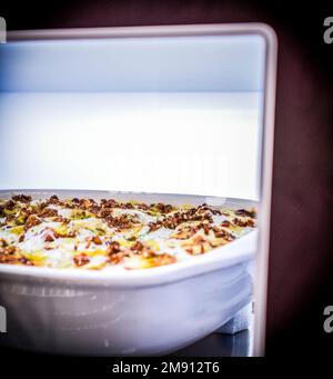Una vista parziale di un contenitore refrattario bianco all'interno del forno con lasagne in cottura Foto Stock