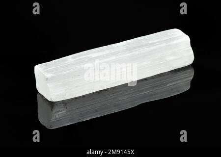 Bianco Selenite Crystal Rod primo piano su sfondo nero con riflessione. La selenite è una varietà di gesso minerale Foto Stock