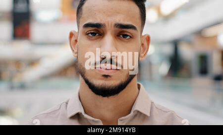 Primo piano del volto sconvolto giovane uomo triste frustrato millenario ragazzo guardando la fotocamera grave ispanico maschio che ha pensieri negativi depressivo umore Foto Stock