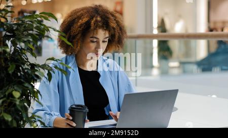 Occupato serio focalizzato ragazza americana millenaria africana business donna freelance manager specialista seduto al tavolo in caffetteria lavorare con il computer portatile Foto Stock
