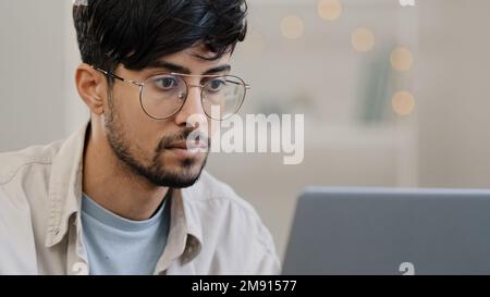 Serio maschio faccia arabo ispanico uomo portatore ragazzo che lavora con il laptop sente lo stress che soffre di mal di testa toglie gli occhiali sfrega gli occhi preoccupati Foto Stock