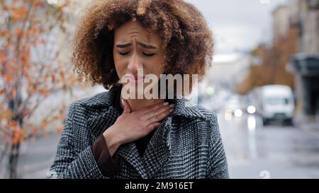 Ritratto afro americano che soffre di tonsillite angina in piedi all'aperto ritratto donna malsana toccare collo sente disagio sentimenti dolorosi Foto Stock