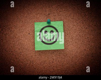 Una nota di carta verde stropicciata con il volto sorridente fissato a un corkboard. Primo piano. Foto Stock