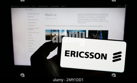 Persona in possesso di smartphone con il logo della società svedese di telecomunicazioni Ericsson sullo schermo di fronte al sito Web. Messa a fuoco sul display del telefono. Foto Stock