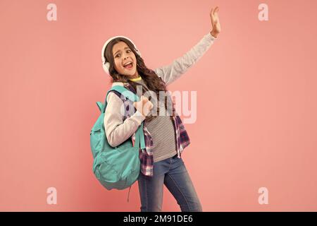 il bambino scioccato ascolta la musica nelle cuffie e porta lo zaino su sfondo rosa, vita moderna Foto Stock