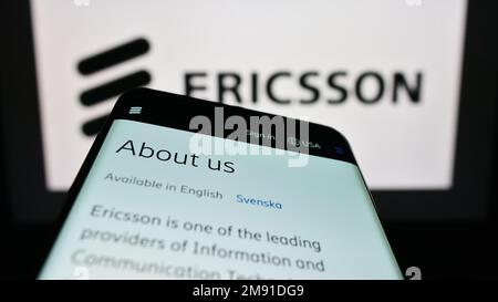 Smartphone con sito web della società di telecomunicazioni svedese Ericsson sullo schermo di fronte al logo aziendale. Messa a fuoco in alto a sinistra del display del telefono. Foto Stock