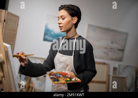 Bruna artista in grembiule pittura su tela in officina Foto Stock