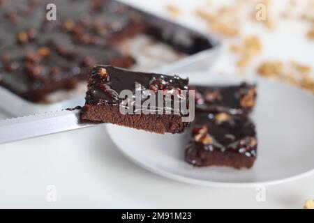 Fetta di Texas Sheet Cake servita su un piatto. Si tratta di una grande e sottile torta al cioccolato sormontata da una ricca glassa di noce al cioccolato. È umido e soffice, w Foto Stock