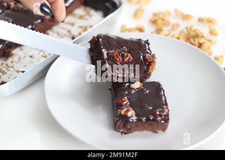 Fetta di Texas Sheet Cake servita su un piatto. Si tratta di una grande e sottile torta al cioccolato sormontata da una ricca glassa di noce al cioccolato. È umido e soffice, w Foto Stock