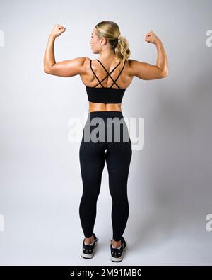 Brawny bella giovane donna che indossa Ponytail mostrando muscoli posteriori Foto Stock