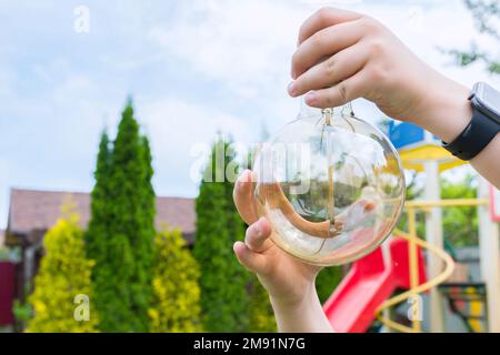 Una lampadina a incandescenza nelle mani di un bambino, un primo piano. Pulizia del giardino Foto Stock