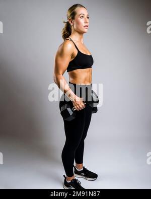 Bella giovane donna muscolare sollevamento Dumbbells circondato da sfondo bianco Foto Stock