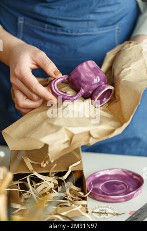 Imprenditore donna irriconoscibile, impaccando una tazza di argilla viola. Imprenditore che lavora a casa con il suo prodotto in ceramica argilla. Vendita online busin Foto Stock