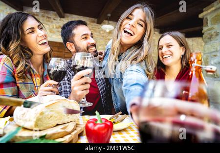 I giovani che si divertono a bere vino fuori lato al patio bar della fattoria - amici felici che si godono il tempo di raccolta insieme in campagna casa - giovani Foto Stock