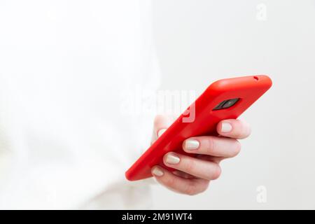 Primo piano della mano femminile utilizzando, tenendo lo smartphone in custodia rossa del telefono su sfondo bianco. Spazio di copia. Foto Stock