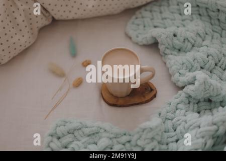 Tazza di caffè con latte sul letto con lenzuola bianche e coperta. Caffè mattutino a letto. Foto Stock
