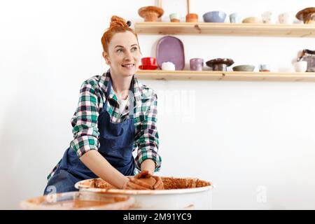 Allegra scultore femminile mentre lei fa pentola di argilla su ruota di ceramica. Idea di piccola impresa e imprenditorialità. Hobby domestico, intrattenimento e leisur Foto Stock