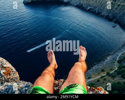 turista seduto in cima a una montagna sopra il mare penzolante piedi all'aperto Foto Stock