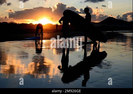 Surfers sulla spiaggia di Caleta de Famara, Playa de Famara, a Lanzarote al tramonto. Foto Stock