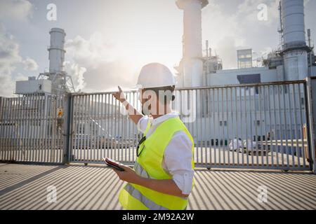 Uomo caucasico ingegnere lavoratore in piedi al di fuori della fabbrica industriale puntando a esso. Foto Stock