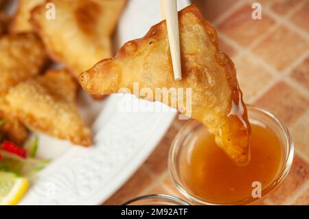 Wontons cinesi con salsa dolce al peperoncino e bastoncini tritare gnocchi fritti asiatici con salsa di soia su piatto bianco. Wontons fritti asiatici. Foto Stock