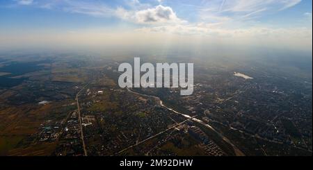 Vista aerea dalla finestra dell'aeroplano ad alta quota della città lontana coperta con strato di smog sottile e nubi distanti in serata Foto Stock