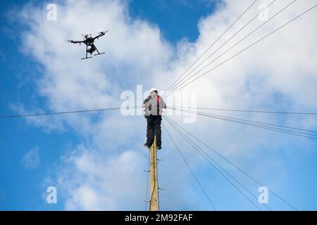 Telecomunicazioni,ingegnere di telecomunicazioni che lavora su palo telegrafo con drone che vola sopra. Tecnologia dei droni, banda larga, 5g, internet... concetto. REGNO UNITO Foto Stock