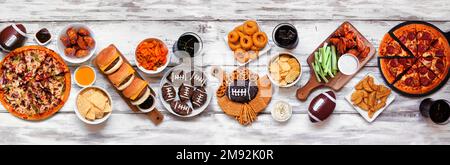 Super Bowl o calcio tavola a tema alimentare scena. Pizza, hamburger, ali di pollo, spuntini e contorni. Vista dall'alto verso il basso su uno sfondo di legno bianco. Foto Stock