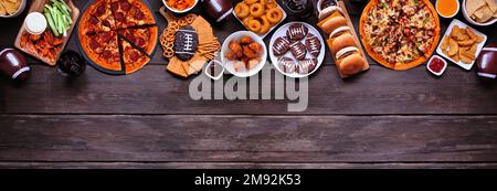 Super Bowl o calcio a tema alimentare bordo superiore. Pizza, hamburger, ali di pollo, spuntini e contorni. Vista dall'alto su uno sfondo di striscione di legno scuro. Foto Stock