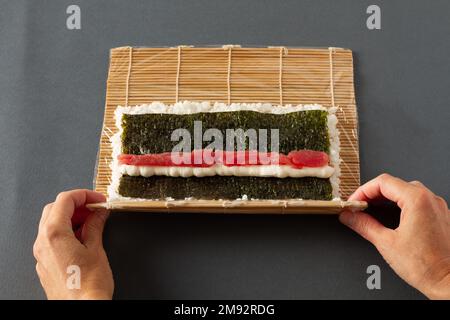 Da sopra di anonimo raccolto che fa sushi con tappeto di rotolamento composto da riso alghe e salmone Foto Stock
