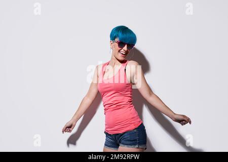 Giovane donna gioiosa in abiti casual in piedi su sfondo bianco con ombra durante la danza Foto Stock